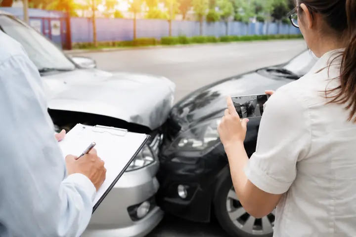 Two people recording damage, one taking a phone photo and one filling in a form beside the cars