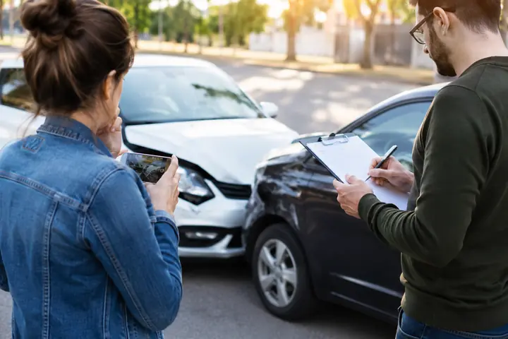 Woman photographing the damage while a man fills in a claim form beside two cars