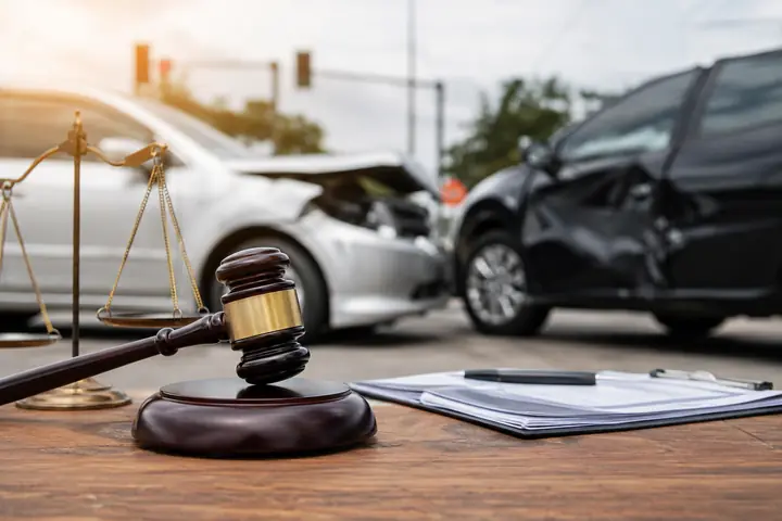 Gavel, scales and papers on a table in front of two cars damaged at an intersection