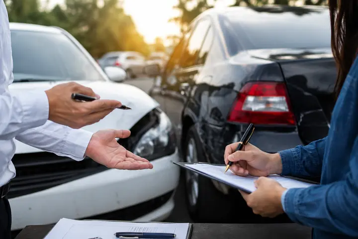 Two drivers discussing a form beside a white car and a black car after a collision