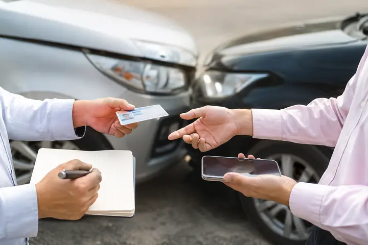 Two drivers swapping a driver's licence and phone details beside their damaged cars